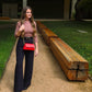 Woman walking outdoors with a red handbag, standing next to wooden planks.